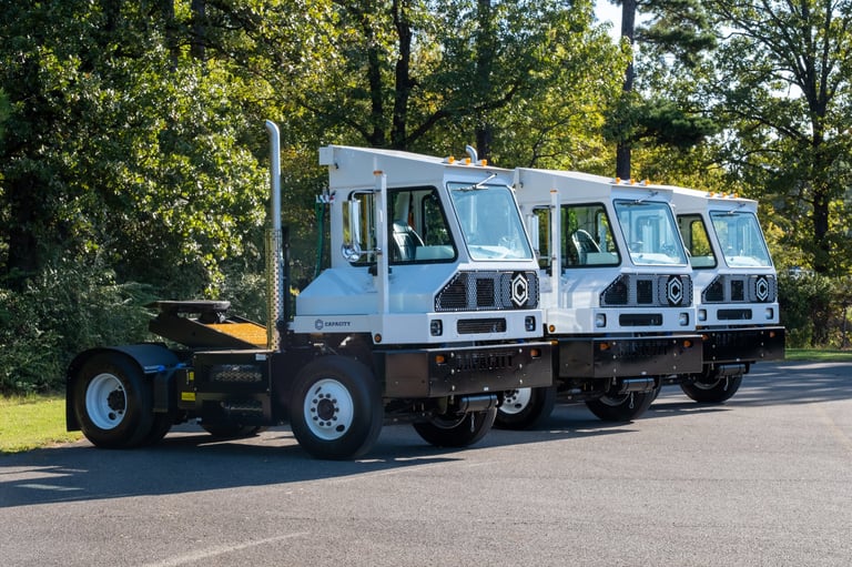 Three white postal delivery trucks lined up on a road with trees in the background